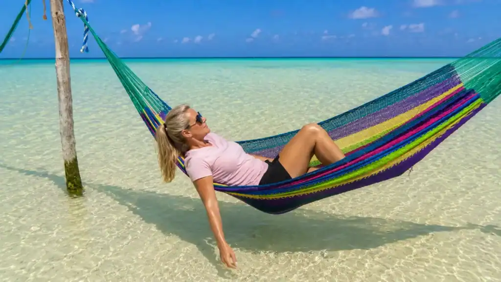 Woman relaxing in a colorful hammock strung over shallow water off Holbox