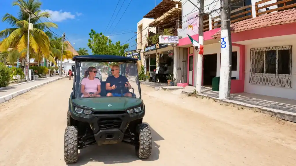 Couple driving a golf cart past pastel hotels in Holbox's town centre