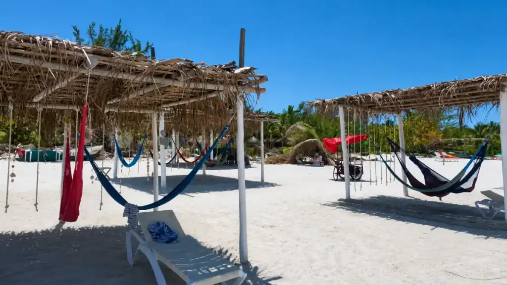 Red and blue hammocks strung beneath thatched palapas on Holbox island's sandy shore