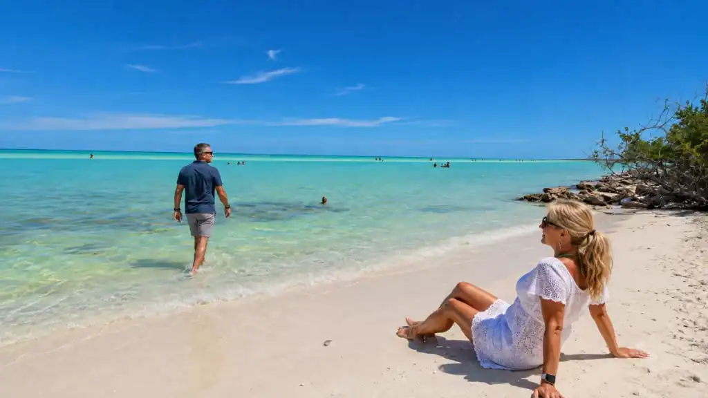 Woman relaxing on the sand as a man wades into shallow water at Punta Mosquito
