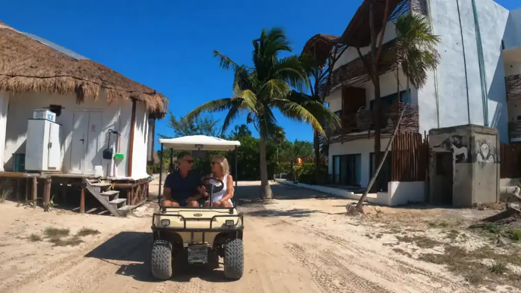 Couple driving a golf cart down a sandy street in Holbox