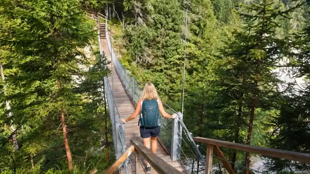 Hiker crosses a steel suspension bridge on a forested gorge trail near Kranjska Gora