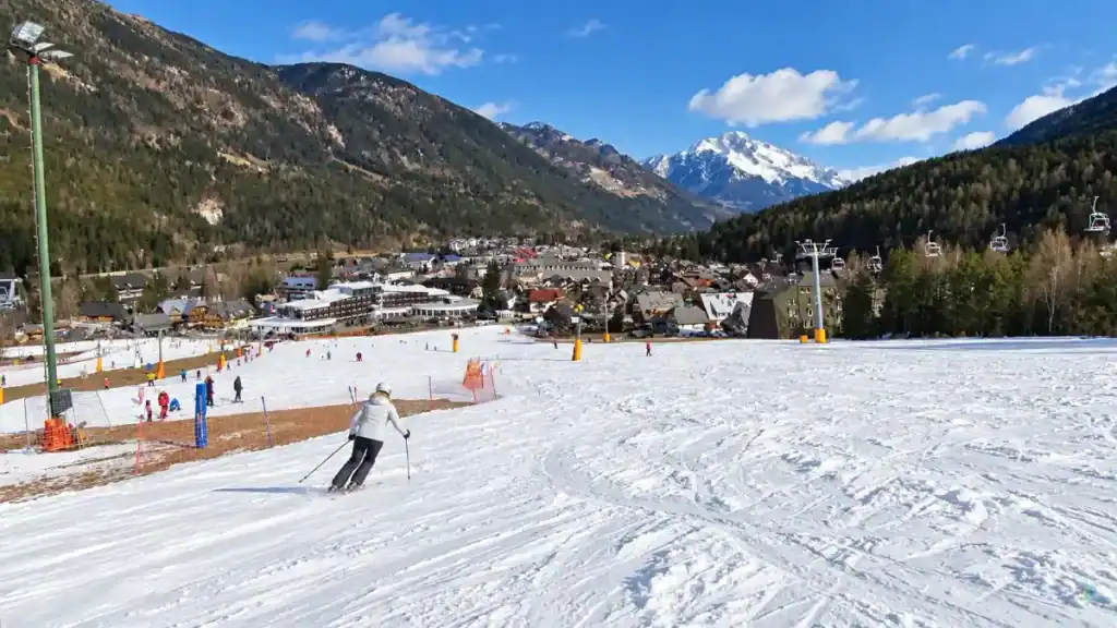 Skier descends the Vitranc slope with the Kranjska Gora village and chairlift below
