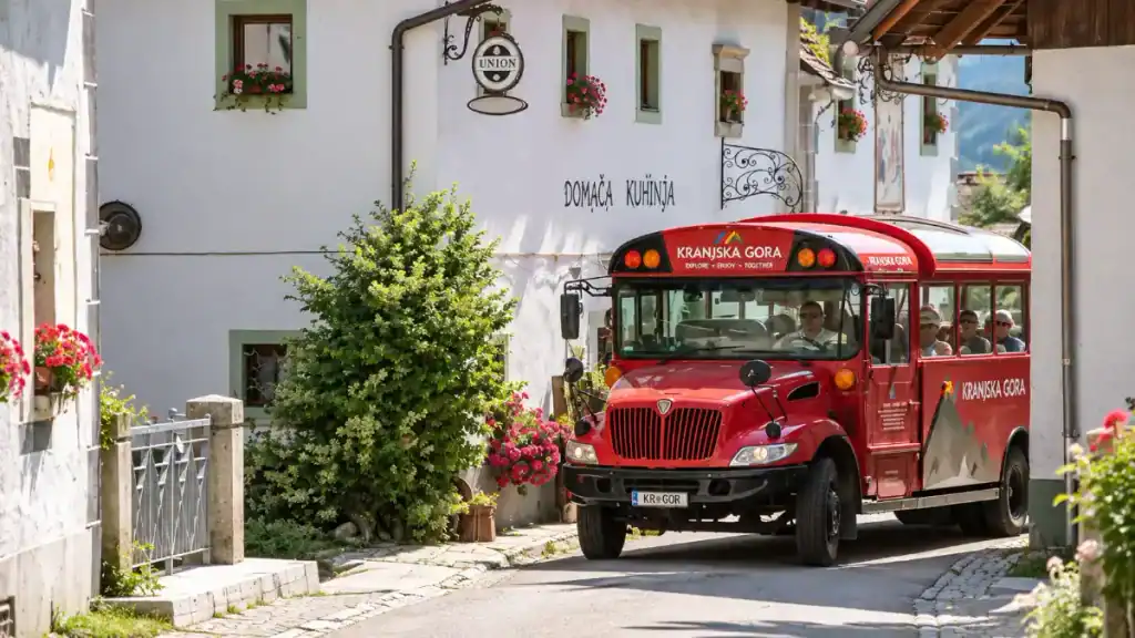 Red Kranjska Gora tourist shuttle passes flower-lined facades on a narrow village street
