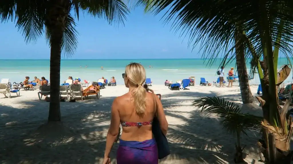 Woman walks toward loungers on Playa Norte, weighing whether is Holbox expensive for a beach day.