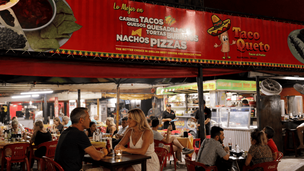 Diners eat beneath a Taco Queto sign advertising tacos and quesadillas