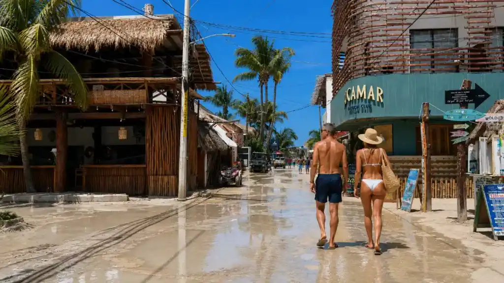 Couple walks past Bocamar Beach Club on wet sandy streets, illustrating is Isla Holbox worth visiting even after rain.