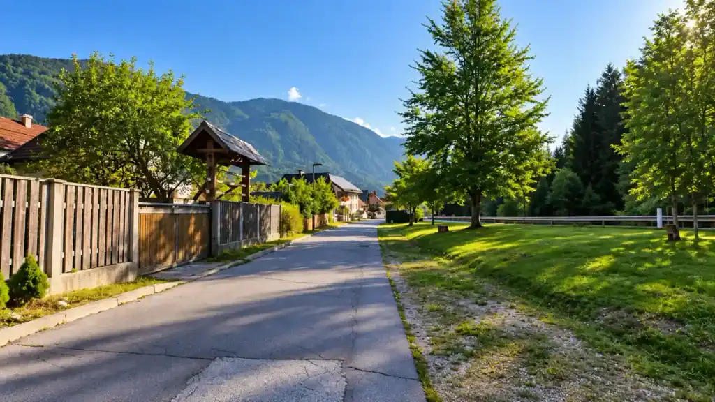 A quiet residential lane with wooden fences opens onto a grassy stretch near Kranjska Gora