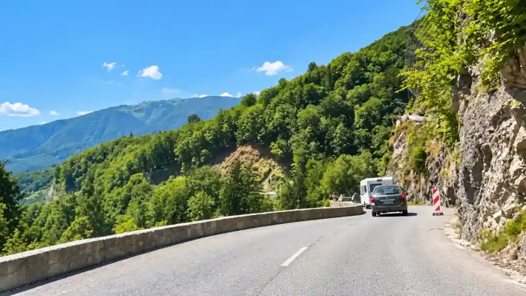 A car and camper van navigate a cliffside curve on the lower stretch of the pass road