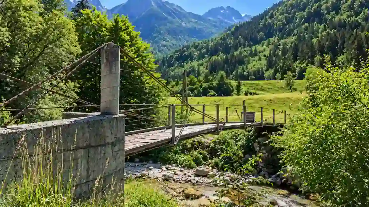 A weathered footbridge crosses a rocky stream in the Soča Valley below distant peaks