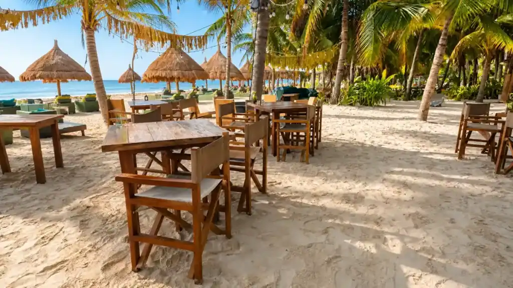 Empty wooden dining tables under palapa umbrellas at a beachfront cafe, part of what shapes how many days in Holbox to spend