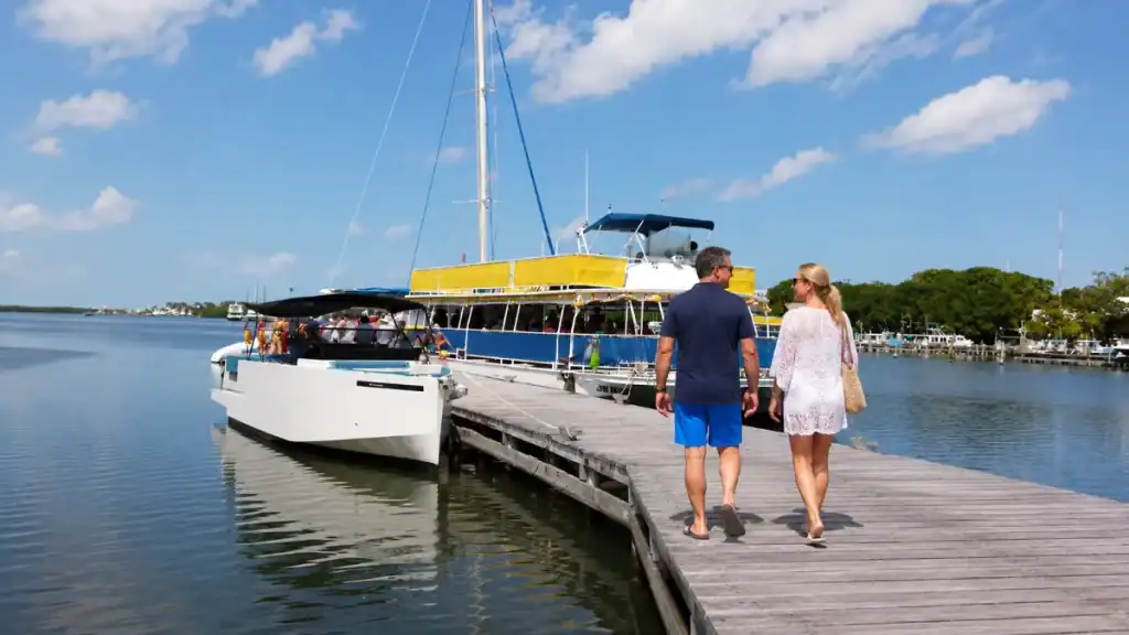 Couple walking a marina dock toward a yellow catamaran tour boat