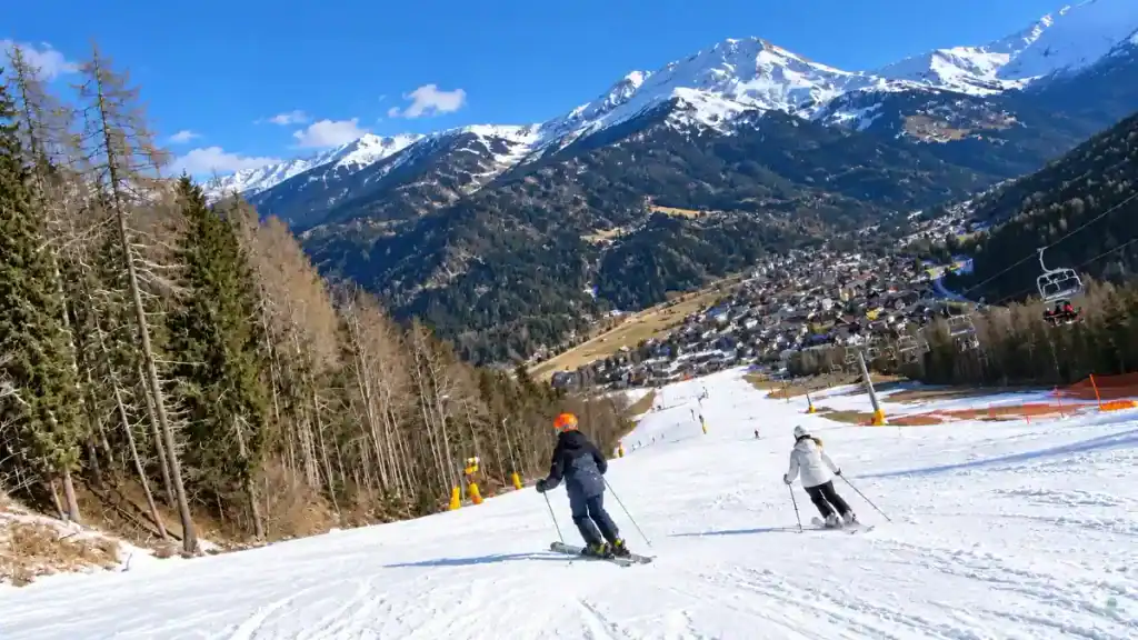 Skiers descend a slope above Kranjska Gora village with a chairlift running alongside the run