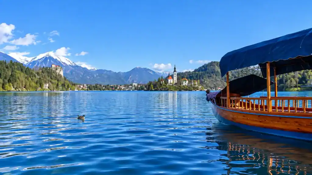 A canopied pletna boat glides across Lake Bled with the island church and castle visible ahead