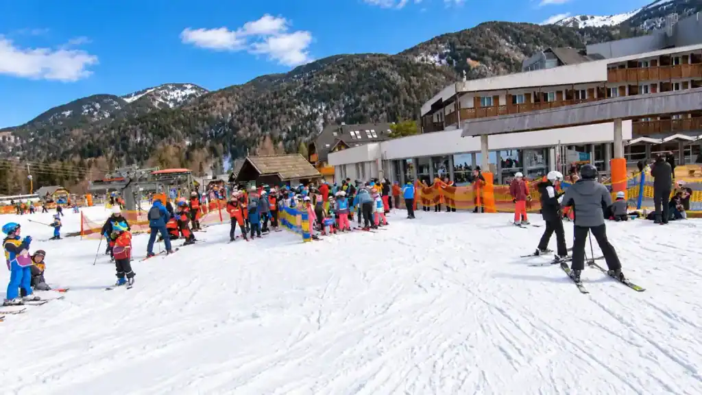 Children's ski school gathers near the base lodge below forested peaks in the Julian Alps.