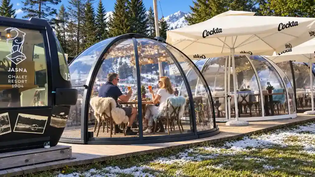 A couple shares drinks inside a glass igloo pod on a terrace near Jasna, Slovenia.