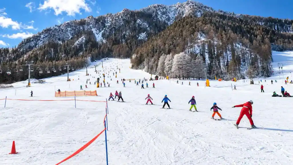A red-suited instructor guides children in a line down the slopes, skiing in Kranjska Gora beneath a chairlift.