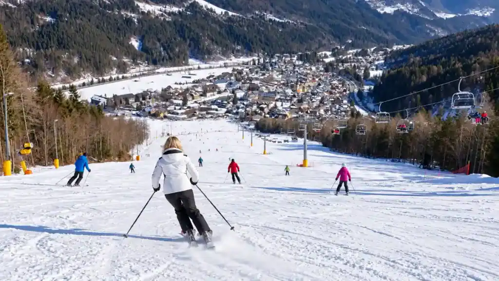 A skier carves down a wide blue piste toward a village nestled in the valley below.