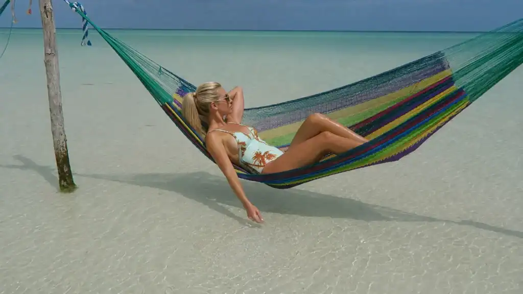 Woman relaxes in a striped hammock strung over shallow water off Holbox